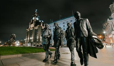 A larger then life statue of the Beatles made from bronze on Liverpool Waterfront at night time