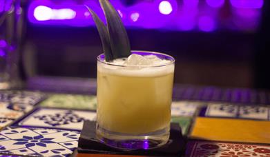 A yellow cocktail with two pineapple leaves sticking out of them.