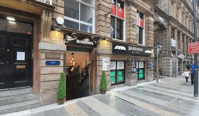 A doorway with two trees by either side of the door. The sign for the bar is black with white writing.